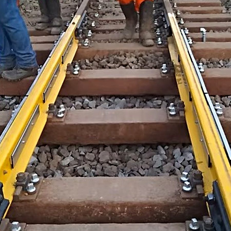 Via férrea em montagem, com perfis amarelos fixados aos trilhos e equipe sobre os dormentes